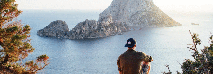 Rear view of man sitting on a rock by the sea